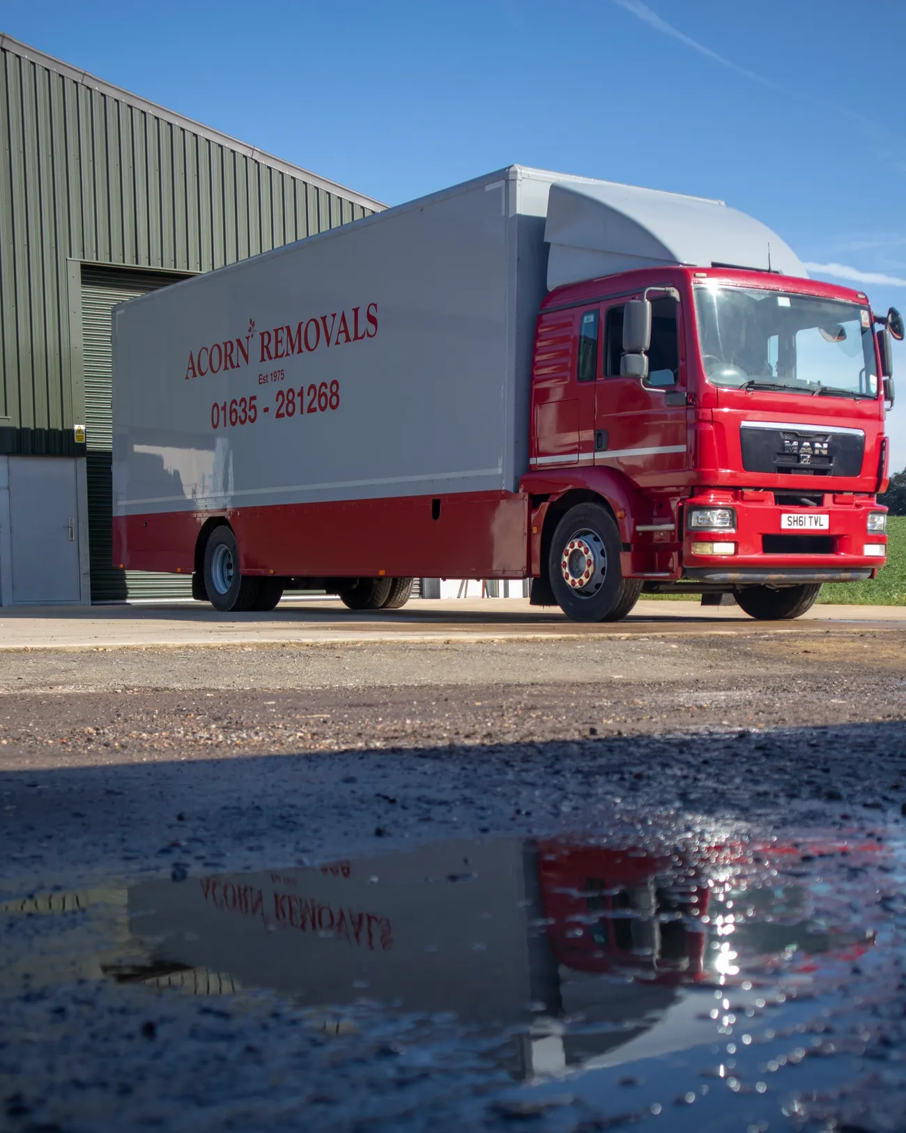 An Acorn removals lorry reflected in a puddle outside the Newbury depot